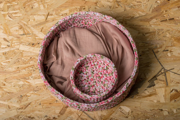 two decorative, knitted, painted in white, pink and green colors baskets for things. A small basket is nested inside a large basket. between them lies beige fabric. Located on Oriented Chipboard. - Powered by Adobe