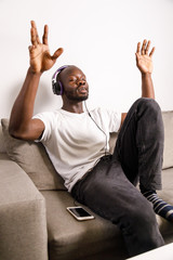 Young african man relaxing with headphones, listening music with eyes closed and gesticulating