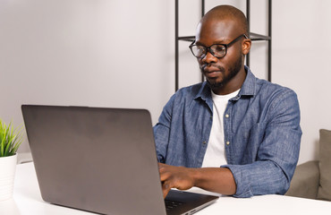 Serious african man wearing glasses watching and working on computer laptop at home
