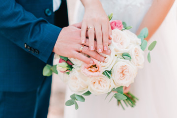 Hands of bride and groom with wedding rings on beautiful bouquet of roses. - obrazy, fototapety, plakaty
