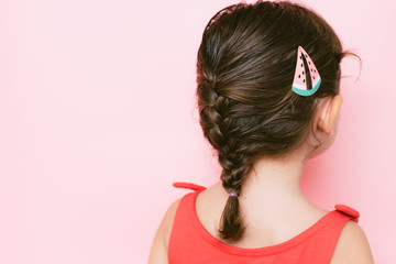 Back view of little girl with braid and hair clip against pink background