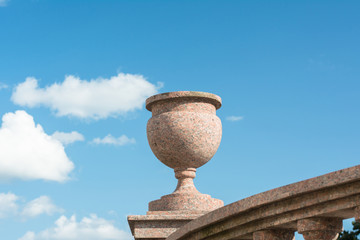 A decorative stone vase stands on a balcony on a city street.  Against the background of a blue sky with clouds