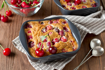 Cherry clafouti in portional ceramic forms on rustic wooden background.