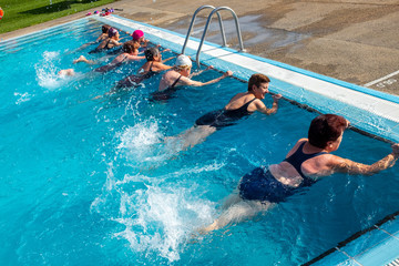 Senior women doing leg exercises in outdoor pool.