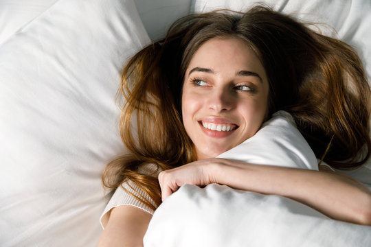 Happy brunette woman waking up after sleep, lying in bed in the morning