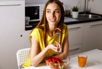 Young brunette woman in yellow t-shirt having healthy breakfast at home