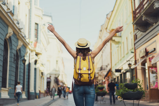 Back view of a young woman traveler with a backpack on her shoulder out sightseeing in a foreign city, stylish female foreigner examines architectural monument during her long-awaited summer vacation
