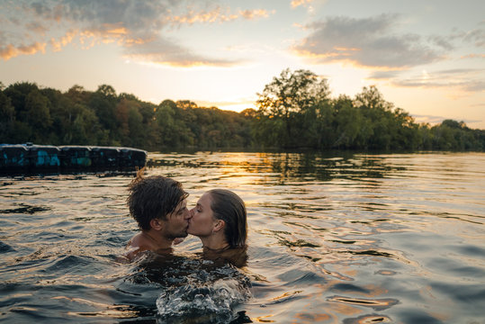 Young couple swimming in lake, kissing at sunset