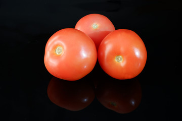 Three fresh ripe tomatoes on black glossy background with reflection