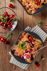 Cherry clafouti in portional ceramic forms on rustic wooden background.