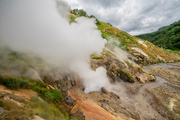 Geyser eruption in the Valley of Geysers in Kronotsky Nature Reserve, Kamchatka Peninsula, Russia. Colorful hill slope of Geysernaya River. Volcanic clay, and geothermal waters surrounding the scene. 
