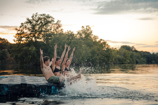 Friends having fun at the lake, sitting on bathing platform, splashing water