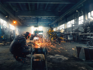 man working with angle grinder metal cutting sparks fly in big hangar