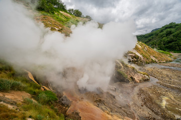 Geyser eruption in the Valley of Geysers in Kronotsky Nature Reserve, Kamchatka Peninsula, Russia. Colorful hill slope of Geysernaya River. Volcanic clay, and geothermal waters surrounding the scene. 