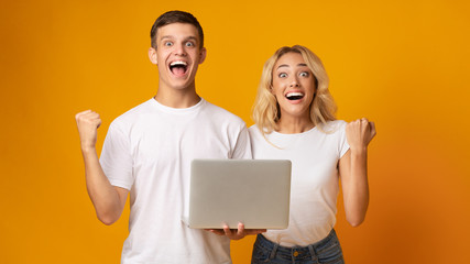 Excited couple of young people celebrating win with laptop