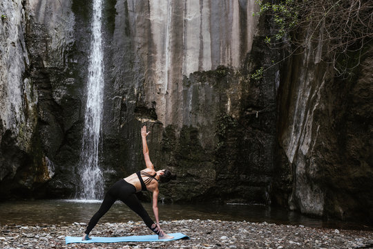 Woman practicing yoga at waterfall, triangle pose