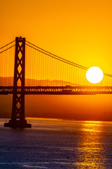 Beautiful summer morning sunrise behind mountain in California gives silhouette to the iconic Oakland Bay Bridge in San Francisco over the ocean.Famous travel location landmark in the west coast city.