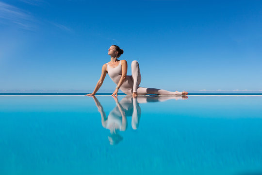 Beautiful young woman yoga instructor doing anantasana sitting on the edge of the pool enjoying the warm morning sun while relaxing in a sunny country. Yoga and relaxation concept. Copyspace