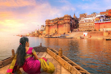 Ancient Varanasi city architecture with Ganges river bank. Indian female tourist enjoy boat ride on...