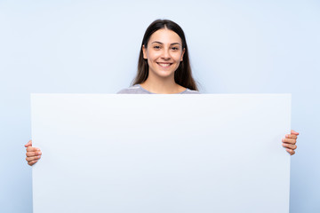 Young brunette woman over isolated blue background holding an empty white placard for insert a...