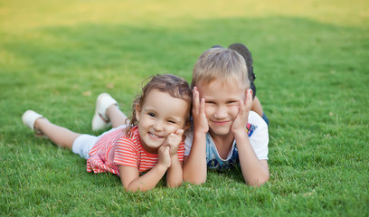 Naklejka na ściany i meble Portrait of a smiling little girl and boy lying on green grass.