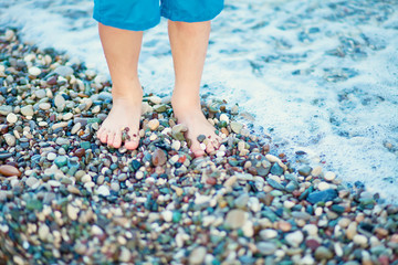 Kid's feet standing on the beach near by the sea.