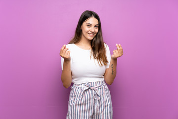 Young woman over isolated purple background making money gesture