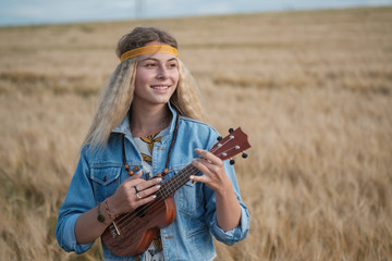 young girl in hippie clothes with ukulele guitar on background of Golden field of ripe rye