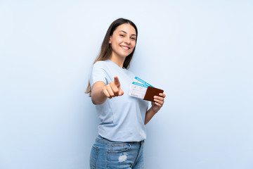 Traveler woman with boarding pass over isolated blue wall points finger at you with a confident expression