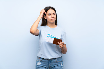 Traveler woman with boarding pass over isolated blue wall having doubts and with confuse face...