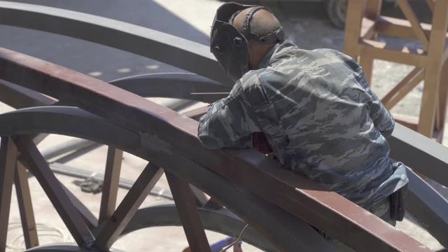 Male welder works by welding with metal construction and taps it with an iron hammer 4k