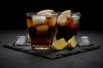 rum and cola Cuba Libre with ice and lemon on dark stone background