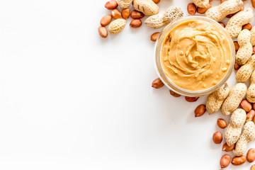 Product for hearty breakfast with peanut butter in bowl near nuts on white background top view...