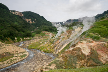 Panorama of the main geyser wall in the Valley of Geysers in Kronotsky Nature Reserve. Slope descending to Geysernaya River, steaming hot springs, mud volcanoes, colorful clay, geothermal waters.