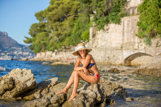 Good looking young woman, sitting on rocks in the sea, enjoying the sun