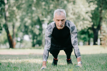 handsome mature sportsman in sportswear doing push ups on lawn in park