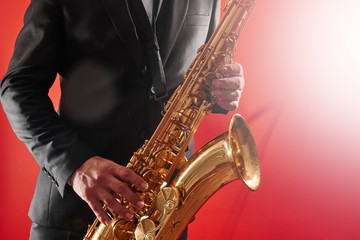 Portrait of professional musician saxophonist man in  suit plays jazz music on saxophone, red background in a photo studio