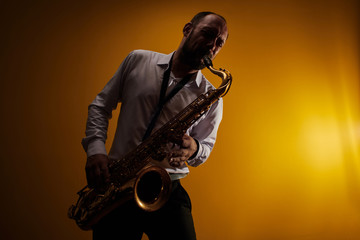 Portrait of professional musician saxophonist man in  white shirt plays jazz music on saxophone,...