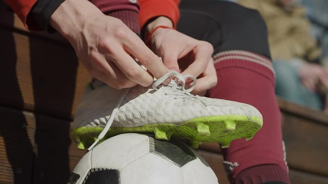 Guy tying his shoelaces on soccer shoes on the street. Hands, feet and ball close in sunlight. Stop the soccer ball with your foot. Street football. Slow motion, 4K