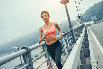 Life is a marathon. Full length of young and confdent blonde woman in sports clothing jogging on the bridge