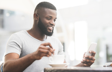 Bearded african man with cup of coffee reading on cellphone