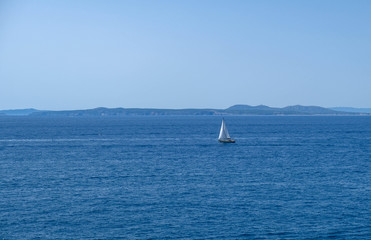 Single white boat sailing on calm water in a sunny day along the coast of the Mediterranean on the background of the islands. Water activities, vacation at sea, happy holidays.