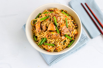 Stir-Fried Noodles with Chicken and Vegetables in a White Bowl with Chopsticks Directly Above Photo.