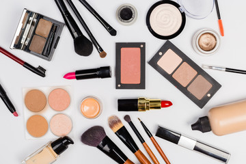 A pink makeup bag with cosmetic beauty products spilling out on to a light  background, with empty space at side