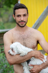 portrait of handsome shirtless man holding a white little dog