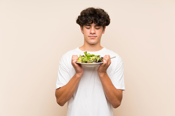 Young man with salad over isolated green wall