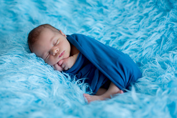 Cute baby boy, peacefully sleeping wrapped in blue wrap