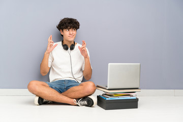 Young man with his laptop sitting one the floor with fingers crossing