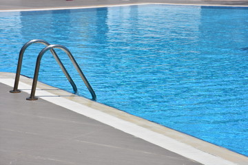 Close up shot of a blue color swimming pool with metal ladder. Modern swimming pool
