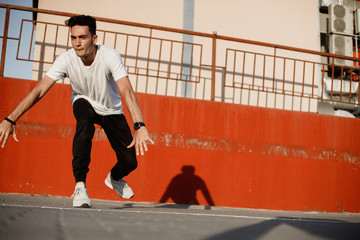 Stylish young guy dressed in jeans and white t-shirt is dancing brakedance in the street against a painted concrete wall in the sunny day